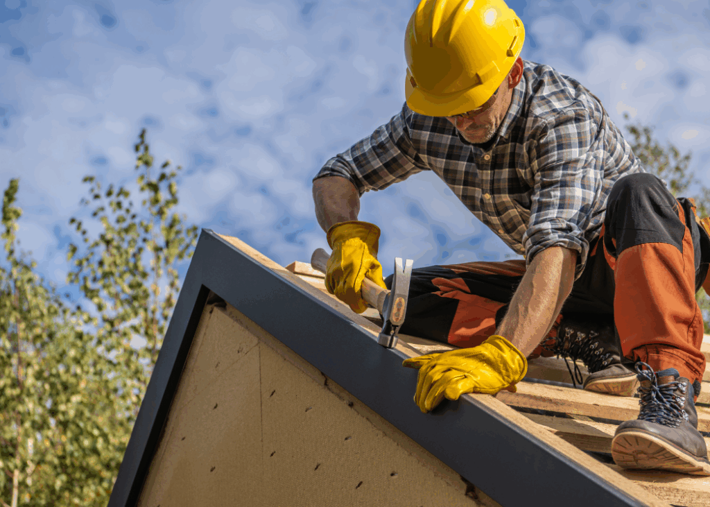 A man wearing a hard hat and safety glasses is working on a roof, focused on his task.