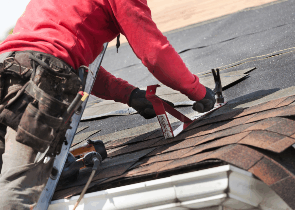 A construction worker in a hard hat and safety glasses is actively repairing a roof.