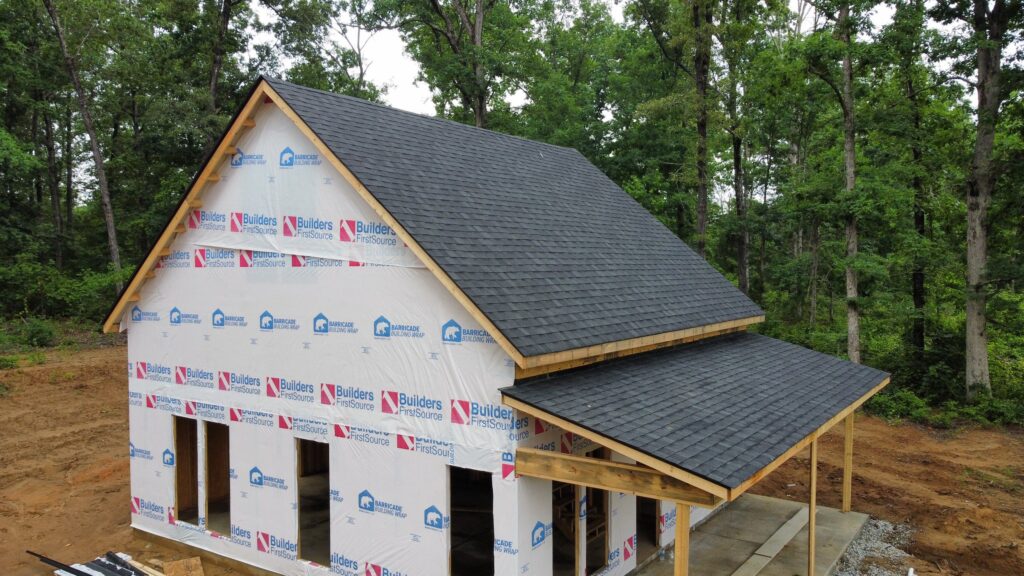 A team of roofing contractors in Charlotte, NC, installing shingles on a house under a clear blue sky.